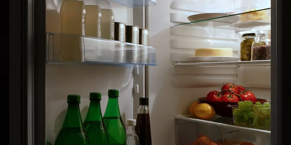 Refrigerador abierto con frascos, verdura y botellas